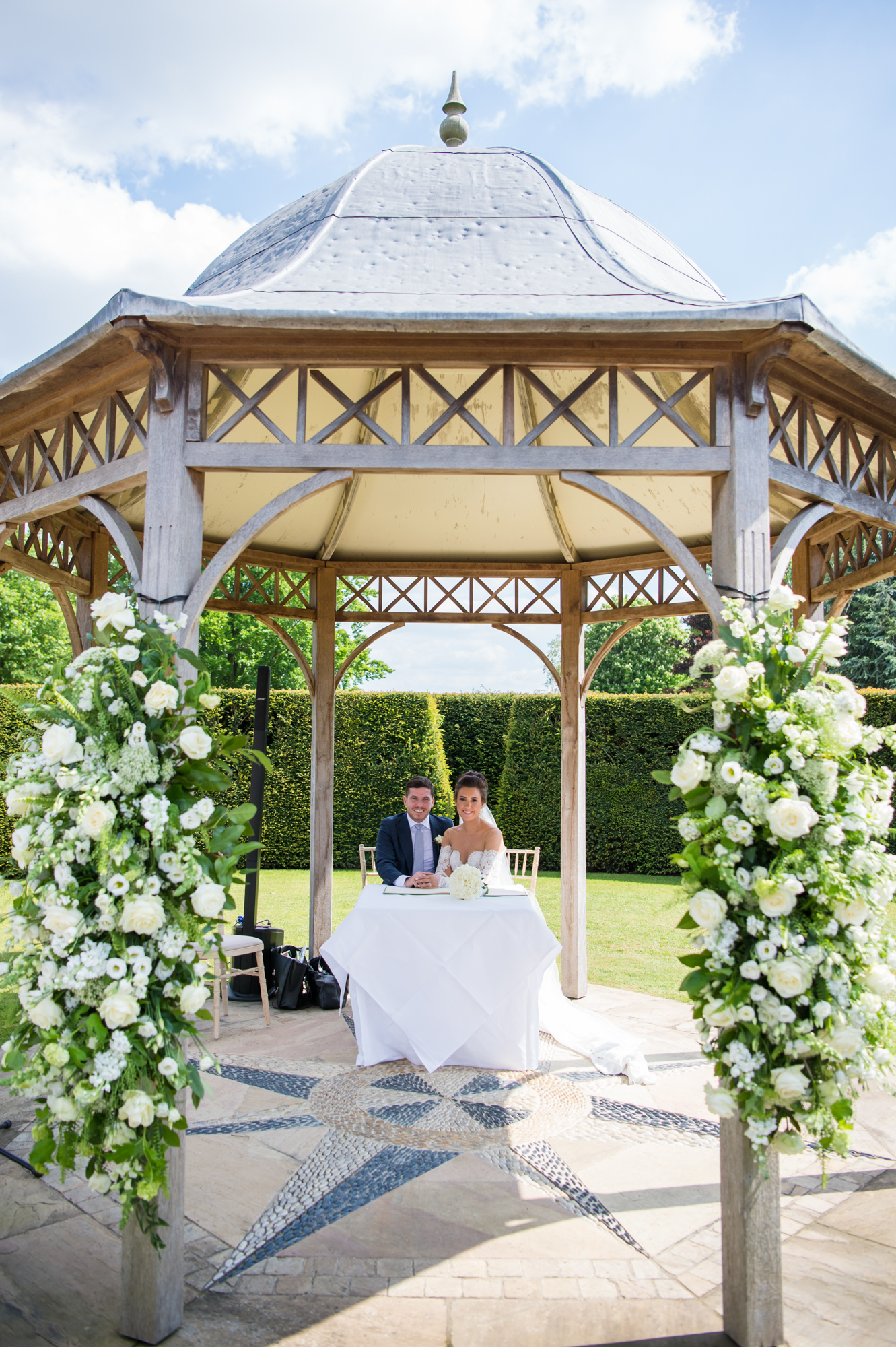 A bride and groom under a timber pagoda decorated with florals at Chippenham park